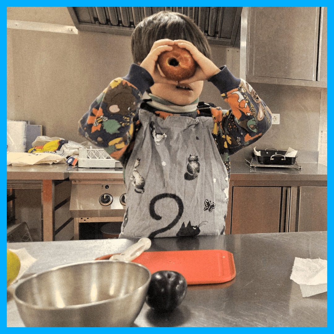 Een kind in de keuken dat een schort draagt, gebruikt een appel als telescoop